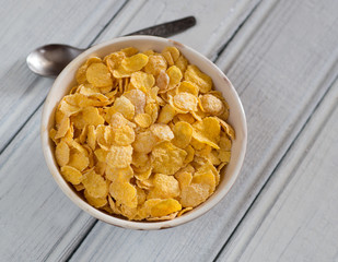 Bowl with cornflakes on white wooden background