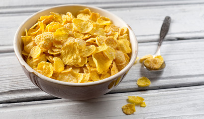 Bowl with cornflakes on white wooden background