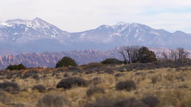 Panning view from vehicle looking at fins and the La Sal Mountains in the desert near Moab Utah.