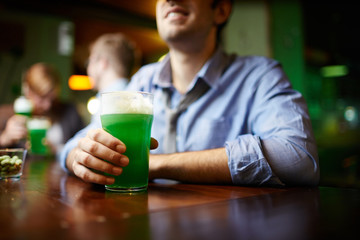 Glass of beer on bar counter held by young man spending leisure in pub