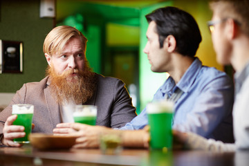 Bearded man with beer discussing plans for night with his friends in bar