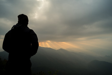 Silhouettes young man stands at the light from clouds. The beam is beautiful