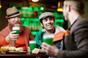 Friendly men with beer sitting in pub at leisure and having talk by table