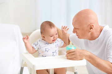 Senior man giving drink to his little grandchild at home