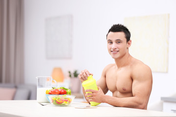 Obraz na płótnie Canvas Handsome muscular young man drinking protein shake in kitchen