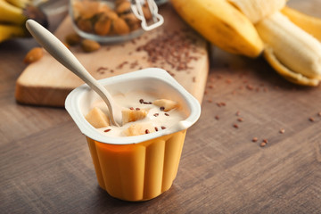 Plastic cup of yummy banana yogurt with flax seeds on wooden table