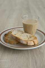 MILK COFFEE ON WOOD TABLE
Two brown crusty sliced french toasts are served in a plate with milk coffee on a wood table.