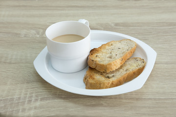 MILK COFFEE ON WOOD TABLE
Two brown crusty sliced french toasts are served in a plate with milk coffee on a wood table.