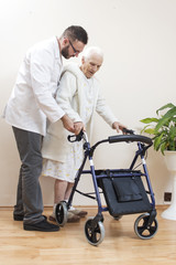 1.	Pielęgniarz pomaga bardzo starej kobiecie iść przy pomocy balkonika rehabilitacyjnego  do chodzenia. - obrazy, fototapety, plakaty
