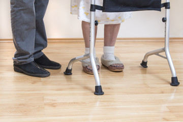 4.	Nogi bardzo starej kobiety w białych skarpetkach i pantoflach. Staruszka uczy się chodzić przy pomocy chodzika rehabilitacyjnego. - obrazy, fototapety, plakaty