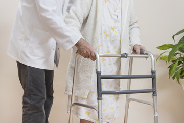 Pielęgniarz pomaga bardzo starej kobiecie iść przy pomocy balkonika rehabilitacyjnego  do chodzenia.