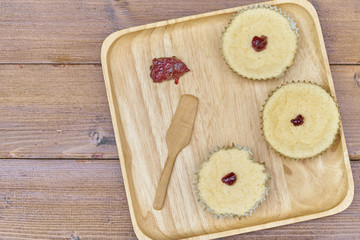The view from the top, snack or breakfast in wooden plate with three cup cakes and jam on wooden background     