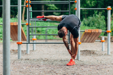 Young caucasian athlete in black sportwear and tattoos, training outdoor and posing