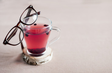 Obraz na płótnie Canvas Blueberry tea in a glass cup and with glasses in a brown frame on it, space for text. anthocyanin to strengthen vision