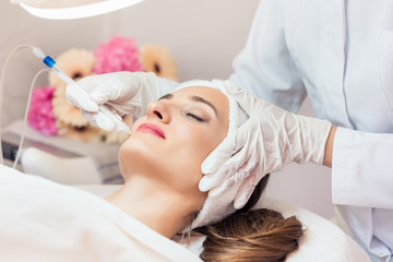 Beautiful woman relaxing during non-invasive facial treatment for rejuvenation in a contemporary...