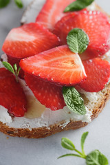 Close-up of a sweet sandwich with fresh strawberry, cream cheese, honey and mint on the white marble.