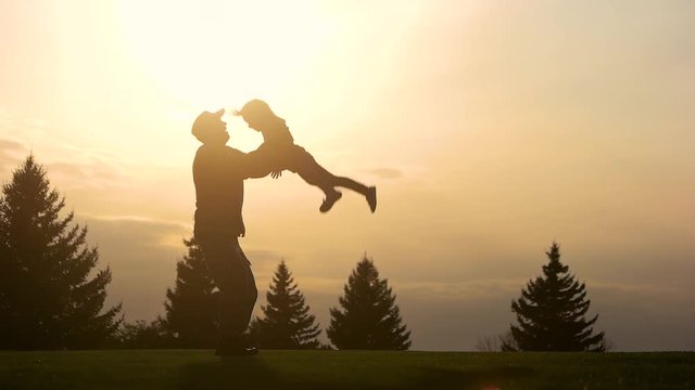 Silhouette of father holding little baby in his hands on sunset. Throwing up a child in the evening.
