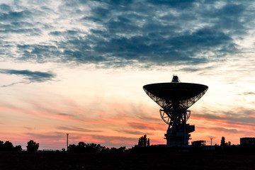 huge white radio telescope of a satellite dish against the sky during sunset