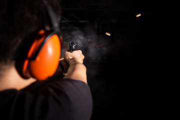 man shooting pistol gun, fire bullet, and wear orange ear cover in shooting range