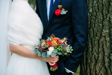 The bride in a white dress and groom in a blue suit are standing in the room and holding a wedding bouquet