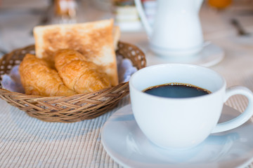 Cup of coffee. Breakfast with coffee and croissants in a basket on table.