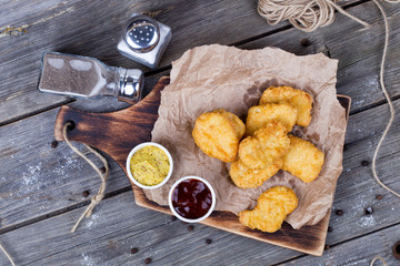 Wooden board with tasty chicken nuggets and sauces on table