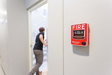 The man running open emergency exit door is and fire alarm on the wall next to the door.