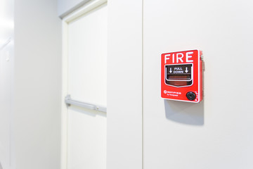 The hand of man is pulling fire alarm on the wall next to the emergency exit door.
