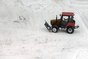 Red tractor cleaning the streets of large amounts of snow in city after snowfall. Winter time...