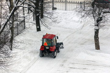 Red tractor cleaning the streets of large amounts of snow in city after snowfall. Winter time...