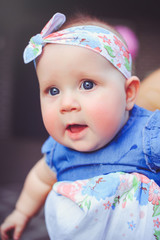 the portrait of a six-month-old child rejoices, is dressed in a blue dress and a headband, 6 months. Concept education of children, children's goods