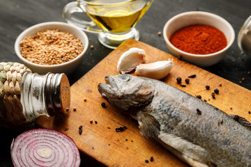 Fresh fish with herbs and spices on vintage cutting board on dark background