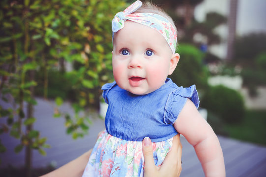 the portrait of a six-month-old child rejoices, is dressed in a blue dress and a bandage on her head, 6 months old mother has on her hands. Concept education of children, children's goods