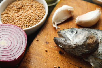 Fresh fish with herbs and spices on vintage cutting board on dark background