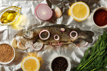 Fresh fish with herbs and spices on crumpled aluminum foil , top view