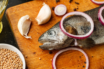 Fresh fish with herbs and spices on vintage cutting board on dark background