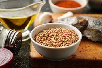 White mustard seeds in a white ceramic bowl on a wooden cutting board. Cooking process