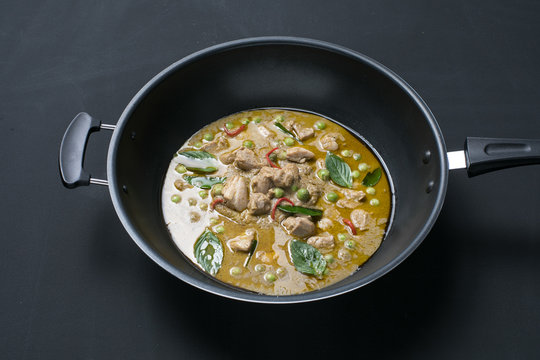 Thai style spicy green curry with pork in a sauce pan on black background.