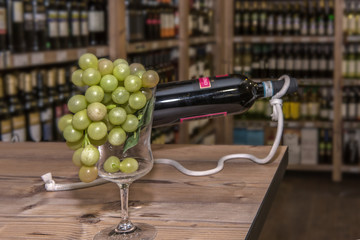 Obraz premium On a table stands a wine bottle and a glass with dékortion. The table is standing in front of a shelf in a beverage market. Focus on the glass in the foreground. Concept: drinks