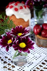 Three spring flowers. Easter cake and red coloured eggs in the background. Easter composition