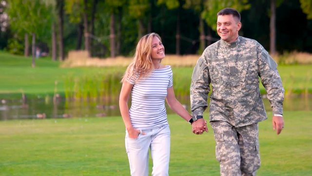 Soldier wear camoubackgrounde in love with a girl. Military man holding hand of his crush and walking in a park.