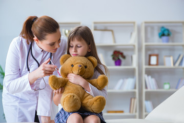 Woman female doctor examining little cute girl with toy bear