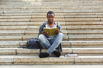 Fototapeta na wymiar Concentrated african-american student reading book on university stairs