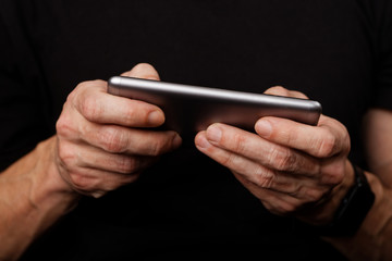 Closeup mans hand using smartphone on black background. Shallow focus.