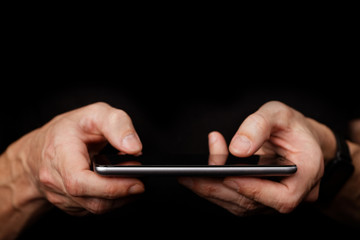 Closeup mans hand using smartphone on black background. Shallow focus.