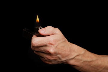 Closeup mans hand holding a burning metal gasoline lighter against black background