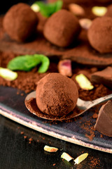 Chocolate truffles covered with cacao powder, pistachio nuts, chocolate and mint on a dark wooden board