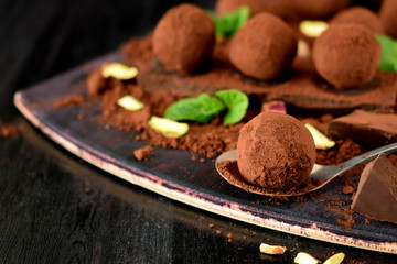 Chocolate truffles covered with cacao powder, pistachio nuts, chocolate and mint on a dark wooden board