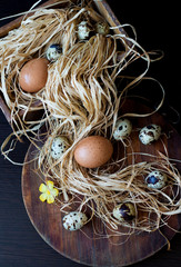 chicken and quail eggs in a straw on a wooden board