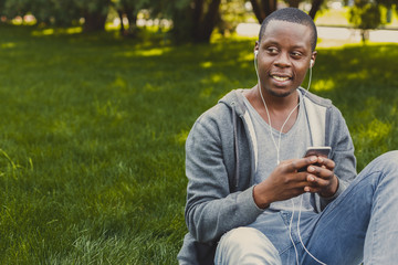 Smiling african-american student listening to music in park outdoors